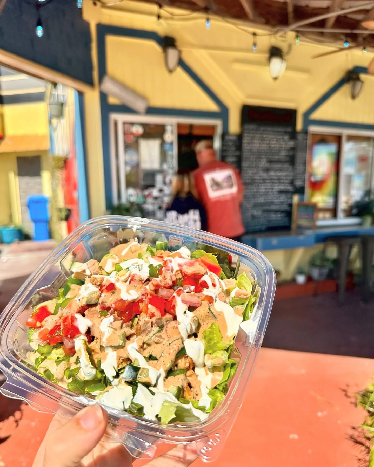 A salad in a to-go bowl held up in front of the order window